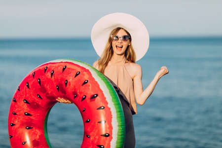 happy girl in a summer hat, dressed in a swimsuit, resting on the sea with an inflatable swimming circle, is happy and shows a winning gesture. summer holidays, travelの写真素材