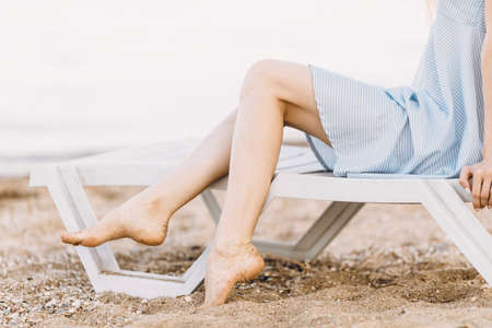 Close-up of women's legs, a woman resting on the sea on a sandy beach, sitting in a chaise longue. Summer vacationの写真素材