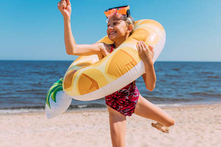 happy little girl in swimming glasses is having fun standing on the beach with an inflatable...