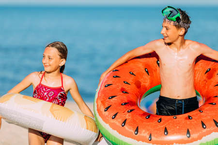 Happy kids brother and sister have fun on the beach with inflatable swimming circles. summer...