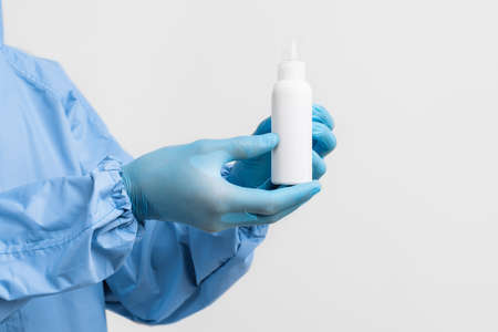 doctor in a protective medical suit against coronavirus, wearing latex gloves, holds a jar of antiseptic disinfectant on an isolated white background. Coronavirus, quarantineの写真素材
