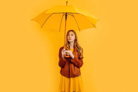 Beautiful girl with a yellow umbrella, with a thoughtful faceの写真素材