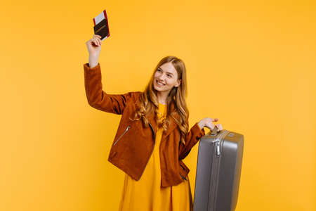 happy attractive smiling girl in a yellow dress and autumn jacket, with a passport and tickets,...
