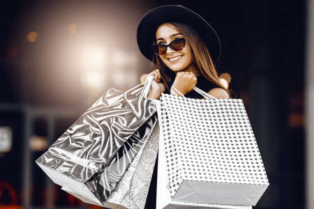 attractive, happy, beautiful young Shopaholic woman, in a black dress, black hat and sunglasses,...