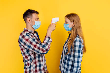 man and a woman in a medical protective mask on their face from the coronavirus, a man checks the...