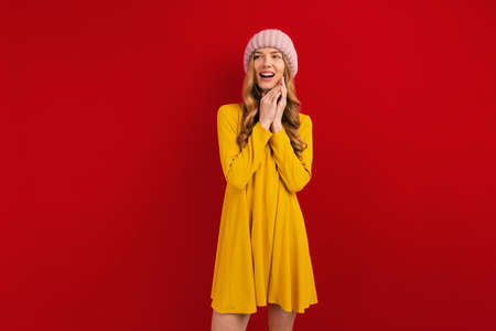 Happy beautiful young woman in a warm hat on her head, on a red background, autumn concept
