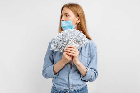 Happy young woman in a medical mask, holding banknotes on a white backgroundの写真素材