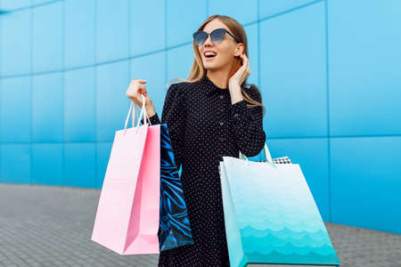Happy young woman in sunglasses and dress with shopping bags on the street in the background of a shopping Mallの写真素材