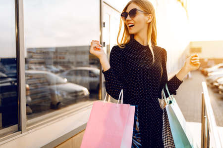 stylish young woman in sunglasses and dress with shopping bags on the street in the background of a shopping Mallの写真素材