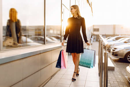 happy young woman in sunglasses and a dress walks after shopping with shopping bags on the street in the background of a shopping centerの写真素材