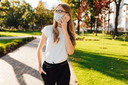 Young business woman in a medical protective mask on her face, talking on a mobile phone, on the street in the cityの写真素材