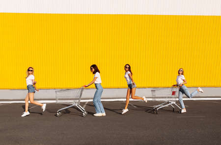 Young happy friends having fun together on shopping carts outdoors. Group of happy girlfriends ride...