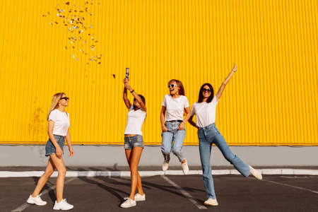 Happy young women friends having fun with confetti on background of yellow wall of shopping mall, concept of funの写真素材
