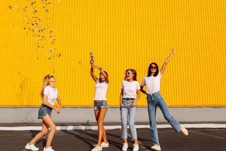 Happy young women friends having fun with confetti on background of yellow wall of shopping mall, concept of funの写真素材