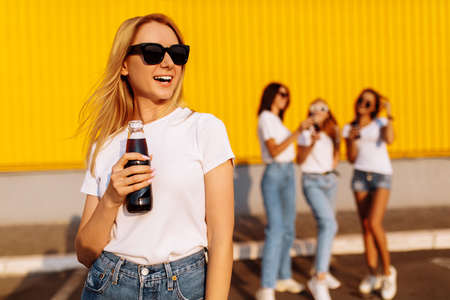 happy young woman in sunglasses drinks a drink on a sunny summer day, in the background with girlfriends near the mallの写真素材