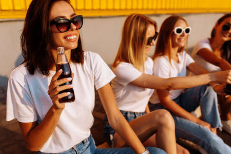 Young happy friends drink a drink and have fun together on a sunny summer day against the background of a yellow wall, the concept of friendship and celebration.の写真素材