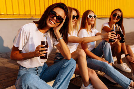 Young happy friends drink a drink and have fun together on a sunny summer day against the background of a yellow wall, the concept of friendship and celebration.の写真素材