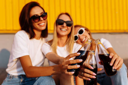 Young happy friends drink a drink and have fun together on a sunny summer day against the background of a yellow wall, the concept of friendship and celebration.の写真素材