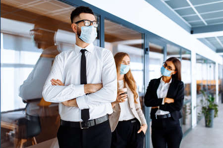 Business colleagues, office workers wearing medical protective masks on their faces chatting during coffee break, coronavirus, quarantineの写真素材