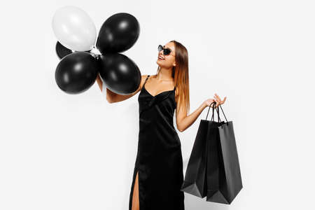 Black Friday sale. Young woman in a black elegant dress, with balloons and shopping bags, on a white backgroundの写真素材