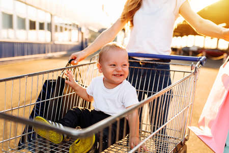 Excited young mother with baby and shopping bags and shopping trolley near mall, family shopping tripの写真素材