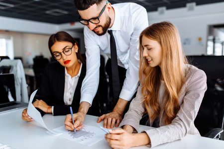 Group of young businessmen working and communicating sitting at office table together with colleagues, business conceptの写真素材