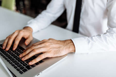 Close up photo of male hands typing on keyboard at indoor workplace