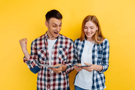 Excited couple, man and woman, holding dollar bills and celebrating on yellow background