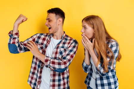Young couple, man and woman showing strength gesture on yellow background