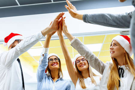 Happy big business team wearing Santa Claus hats demonstrating unity with their hands in the office....