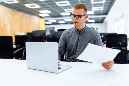 businessman uses a laptop while sitting at his desk. man develops business plans with documents on...