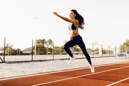 athletic african american woman in sportswear long jump at stadium outdoorsの写真素材