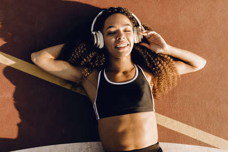 athletic african american woman listening to music on headphones and doing abs workout at stadium at sunrise, healthy lifestyle conceptの写真素材