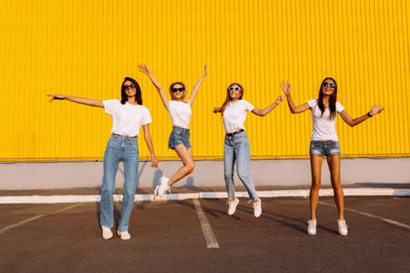 Excited group of friends having fun and jumping against yellow wall background on sunny summer dayの写真素材