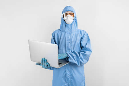 doctor in protective medical suit, mask, glasses and gloves works using a laptop, on an isolated...