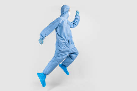 doctor in protective suit, glasses, mask and gloves, rejoices and jumps on white background, coronavirus epidemic conceptの写真素材