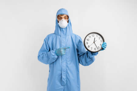 doctor in protective suit, glasses, mask and gloves, points to watch, against white background, coronavirus epidemic conceptの写真素材