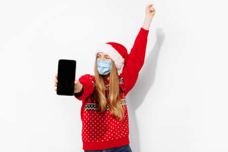 Excited happy young woman wearing santa claus hat and medical protective mask from covid 19,...