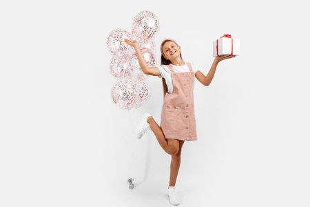 Adorable excited little girl with balloons and a gift, on an isolated white background, The concept of a holiday, Birthdayの写真素材