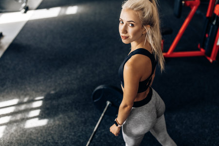 Strong fitness woman, in sportswear, trains with heavy weights in the gym, Sportswoman lifts the...