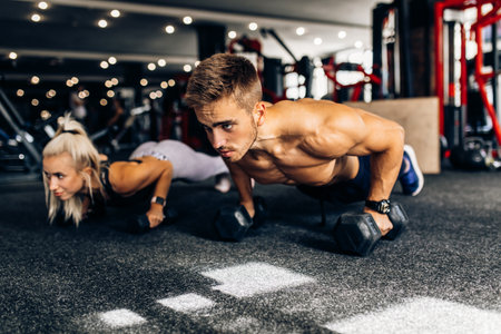 Attractive athletic people, man and woman working out with dumbbells in the gymの写真素材
