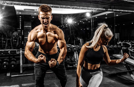 Excited screaming people, muscular man and woman, sportive couple standing in the gym, on black backgroundの写真素材