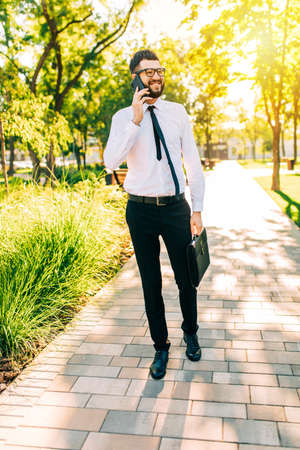 Happy elegant businessman wearing glasses talking on mobile phone while walking around the cityの写真素材
