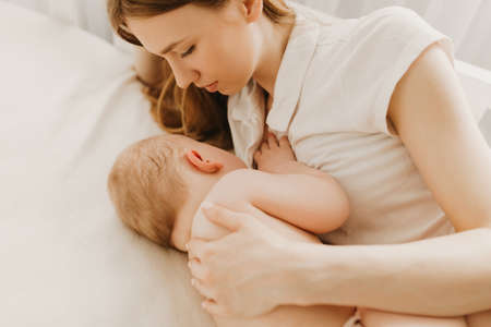 Beautiful young mom and her cute little baby sleeping in bed at homeの写真素材