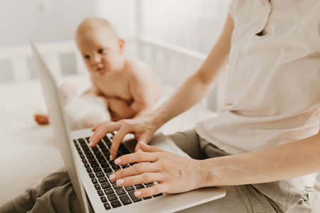 Beautiful young mother works with a laptop and sits with a small child at home, remote work,...