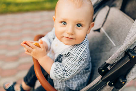A small child sits in a stroller on the street in the park, and waits for mom