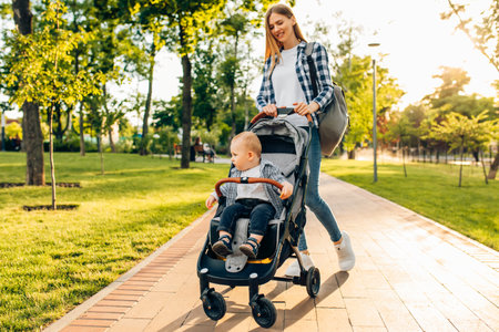 Happy family outdoors, a young mother walks with a little toddler in a stroller in the summer on natureの写真素材