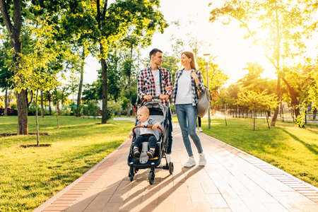 Happy family, dad mom are walking with a little kid in a stroller in the summer outdoors in the parkの写真素材