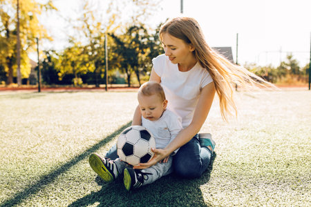Happy young mom with son playing with soccer ball on field, outdoorsの写真素材