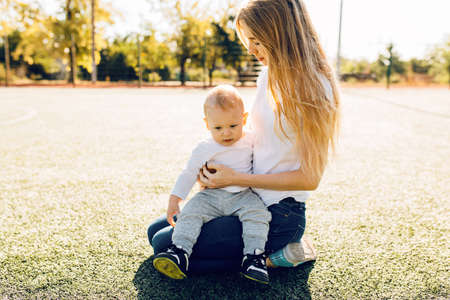 Portrait of happy loving mother and her baby sitting on the lawn in the park outdoorsの写真素材